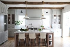 a large kitchen with white cabinets and wooden flooring, along with three bar stools