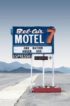 a motel sign sitting on the side of a road with mountains in the back ground