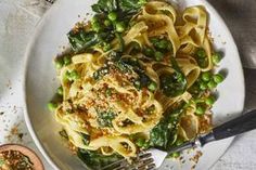 a white plate topped with pasta and peas next to a small bowl of seasoning