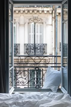 an open window overlooking a balcony with iron railings and white pillows on the bed