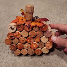 a hand holding a wine cork holder with autumn leaves on it and an orange maple leaf