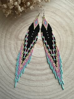 two pairs of beaded earrings sitting on top of a piece of wood next to a plant