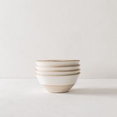 four white bowls stacked on top of each other in front of a plain white wall