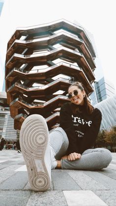 a woman sitting on the ground with her feet up in front of a tall building