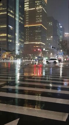 a city street at night with cars driving on the road and buildings in the background