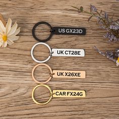 four different metal keychains sitting on top of a wooden table next to flowers