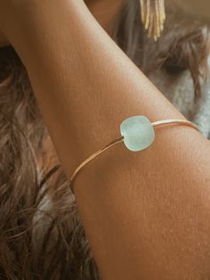 This Seaglass Banle is crafted from beautiful gold filled metal and features a round light blue sea glass bead. With its size of 6,7, or 8” this bangle is perfect for all wrist sizes. It's an eye-catching piece sure to make a statement.