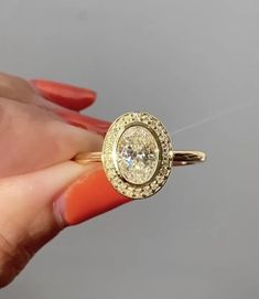 a woman's hand holding an orange ring with a diamond in the center and two rows of diamonds around it