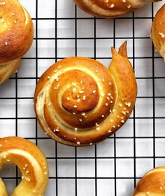 several buns with sesame seeds on a cooling rack, one has a spiral design and the other has white sprinkles