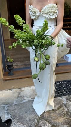 a woman in a white dress holding a bouquet of green flowers and greenery on her lap