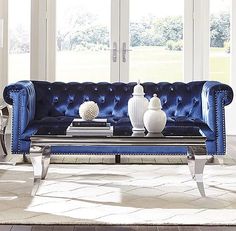 a living room with blue velvet couches and white vases on the coffee table