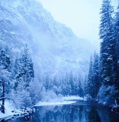 snow covered mountains and trees surrounding a small lake in the middle of a snowy forest