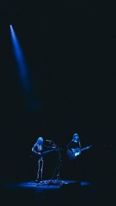 two people on stage playing instruments in the dark with blue light coming from behind them