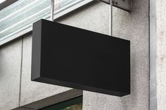 a black square sign hanging from the side of a building next to a glass window