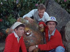 three men in red shirts and white hats posing for a photo with a tortoise shell