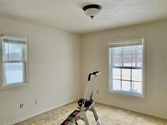 an empty room with two windows and a ladder on the floor in front of it