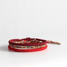 two red bracelets with gold beads on each one and a string attached to the other