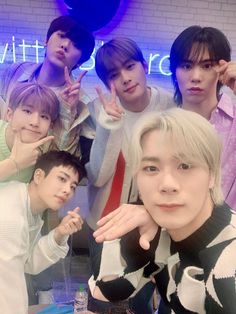 group of young men posing in front of a neon sign with one hand up to the camera