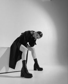 a black and white photo of a woman leaning against a wall with her legs crossed