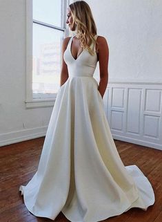 a woman standing in front of a window wearing a white wedding dress with deep v - neck