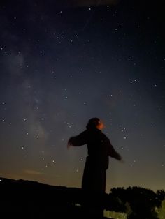 a person standing in the dark with their arms spread out looking up at the stars