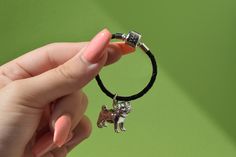 a hand holding a small dog charm on a black cord with a silver bead around it