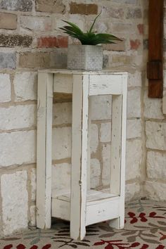 a small white table with a potted plant on top and a brick wall behind it