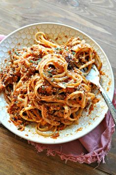 a white plate topped with pasta and sauce on top of a wooden table next to a pink napkin