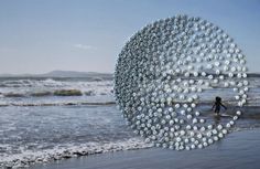 a person walking on the beach next to an art piece made out of plastic balls