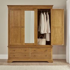 a large wooden armoire with two drawers and a mirror on the door, in front of a white wall