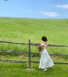 a woman in a white dress is standing near a fence and holding a bouquet of flowers