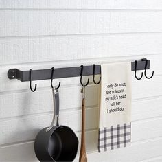 two pots and pans hanging from hooks on a wall next to a kitchen towel rack