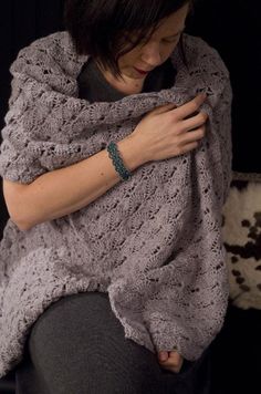 a woman wrapped in a gray crochet shawl with her hands on her chest