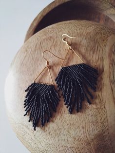 a pair of black beaded earrings on top of a wooden stand with beads hanging from it