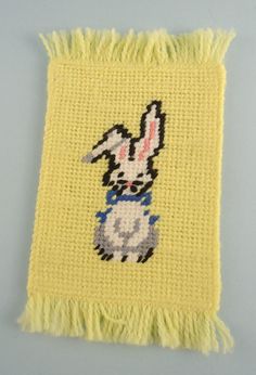 a cross - stitch bunny is sitting on a yellow piece of cloth with fringes around it