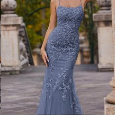 a woman in a blue dress standing next to a stone pillar and looking at the camera