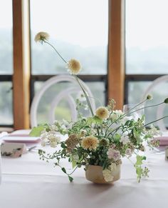 a white table topped with a vase filled with lots of flowers next to two windows