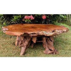 a large wooden table sitting on top of a lush green field next to flowers and trees