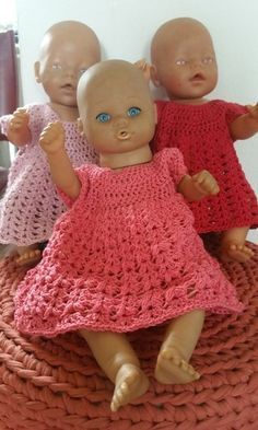 three little dolls sitting on top of a basket with their hands in the air and one doll is wearing a pink crocheted dress