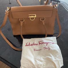 A Salvatore Ferragamo Purse From The Lotty Collection Styled In Pebbled Calfskin Leather With Gold-Tone Hardware And A Fully Lined Interior. This Bag Features 2 Open Pockets With A Flap Secured By Gancio Flip Lock, 1 Interior Zip Pocket And One Front Exterior Zip Pocket. Additional Features Include 2 Rolled Leather Handles With 7.5" Drop. Dimensions 10" Height 13" Wide 5" Deep Bought In Italy New For Work Clothes Accessory But Never Used Because I Prefer Bags With Shoulder Straps Only. Pre-owned Elegant Leather Shoulder Bag, Pre-owned Top Handle Bags For Formal Occasions, Elegant Pre-owned Leather Shoulder Bag, Pre-owned Elegant Top Handle Bag, Elegant Pre-owned Top Handle Bag, Salvatore Ferragamo Bags, Work Clothes, Rebecca Minkoff Mac, Leather Handles