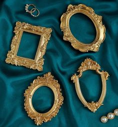 four gold frames with wedding rings on them and one ring in the middle, sitting on a green satin