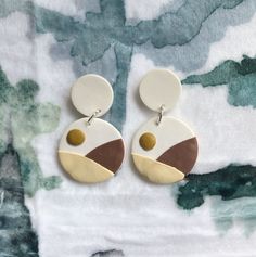 a pair of earrings on top of a white and brown blanket with trees in the background