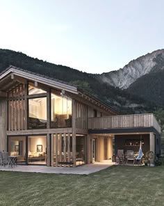 a large wooden house sitting in the middle of a lush green field next to mountains