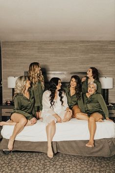 four women in green robes sitting on a white bed with their feet up and smiling at each other