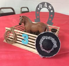 a toy horse in a wooden crate on a red tablecloth with the number 3