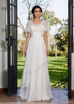 a woman standing in front of an open door wearing a white dress with tiered layers