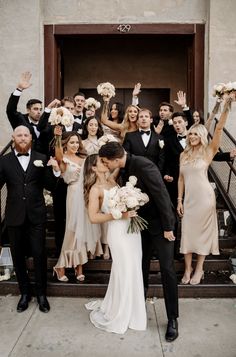 a bride and groom kissing in front of their wedding party