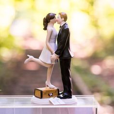 a bride and groom figurine kissing on top of a suitcase