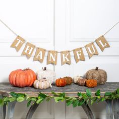 a table topped with pumpkins and bunting banner next to a wooden sign that says, thank you