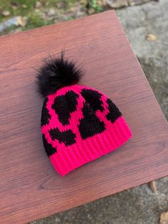 a pink and black knitted hat on top of a wooden table